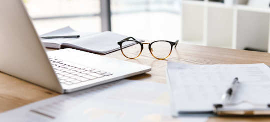 Arbeitsplatz mit Brille, Laptop und Unterlagen - bildlich Arbeitsrecht