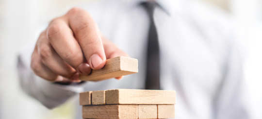 Geschäftsmann stapelt Holzbausteine zu einem Turm - bildlich für strategische Überlegungen bei Schenkungen und Erbschaftssteuer